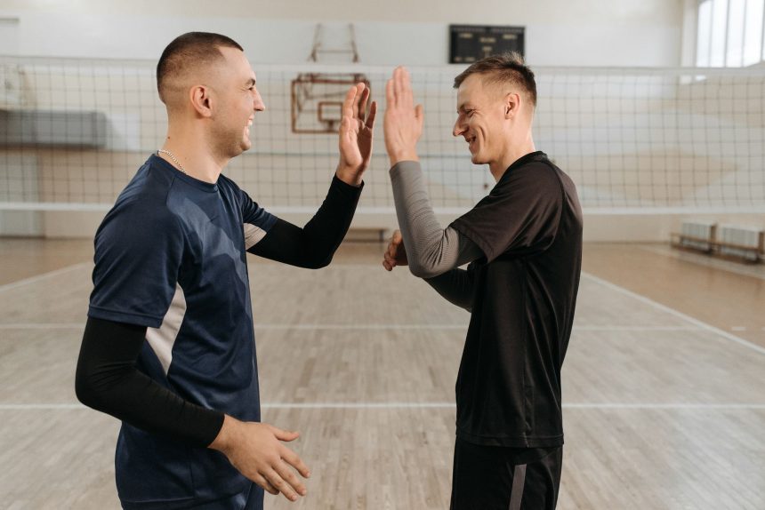 Dois jogadores de vôlei masculino se cumprimentam em comemoração após uma jogada, em uma quadra coberta.