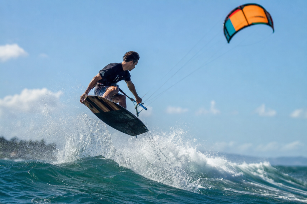 Atleta brasileiro praticando kitesurf em uma onda com vento forte e a pipa no céu