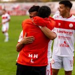 Jogadores de futebol comemoram uma vitória no campo, abraçados e demonstrando alegria.