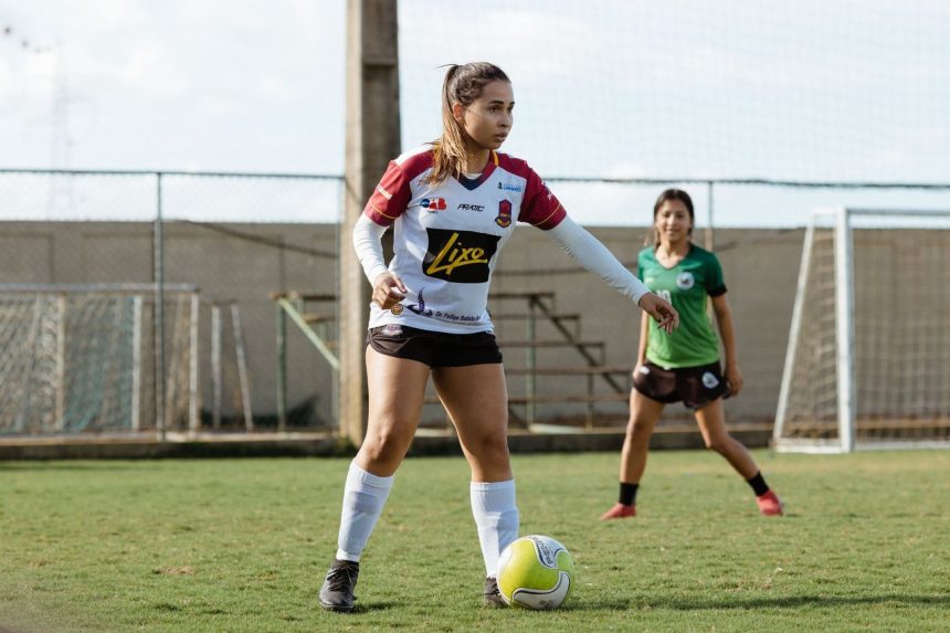 Duas adolescentes disputam uma partida de futebol em um campo ao ar livre.