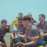 Time de futebol comemora a conquista de um campeonato segurando um troféu em campo