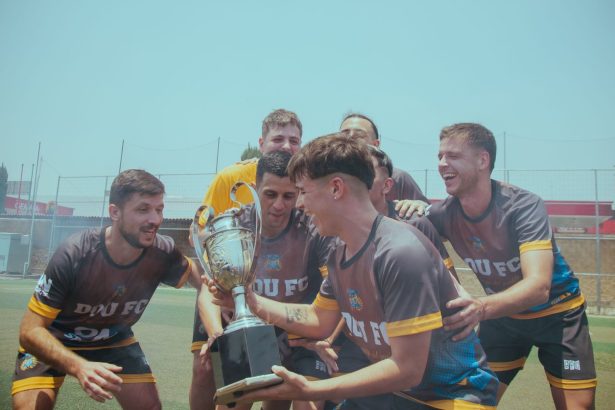 Time de futebol comemora a conquista de um campeonato segurando um troféu em campo
