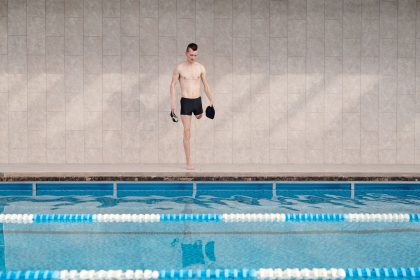 Atleta com prótese em uma perna se prepara para nadar em uma piscina coberta.